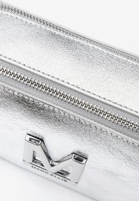 Silberne metallische Leder-Tasche mit einem auffälligen 'M'-Logo aus poliertem Metall und einem Reißverschluss an der oberen Kante.