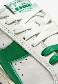 Sneaker bianco in pelle con accenti in suede verde. Caratterizzato da lacci texturizzati, dettagli cuciti e un'etichetta con logo verde e bianco sulla linguetta.