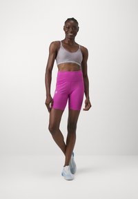 Ljusgrå sportbh med justerbara remmar och logotyp; klarröda högmidjade shorts; vit sportskor med blå accenter.