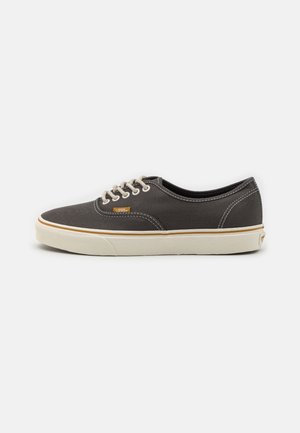 Lavtops grå lærreds-sneaker med hvide snørebånd, hvid gummisål, kontrastsyninger og lille orange Vans-logo tag på siden.