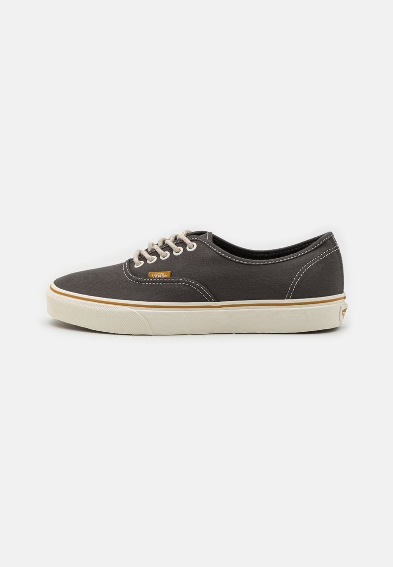 Baskets basses en toile grise avec lacets blancs, semelle en caoutchouc blanche, coutures contrastées et petite étiquette orange avec le logo Vans sur le côté.