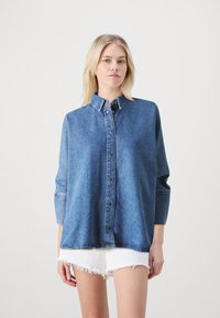 Denim shirt in medium blue with a button-up front, collar, and three-quarter sleeves. Features a slightly oversized fit and straight hem.
