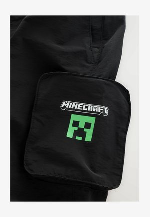 Fekete rövidnadrág nagyméretű zsebbel, a "Minecraft" logójával és egy zöld Creeper arc grafikával. Sima textúra, hétköznapi dizájn.
