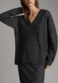 Luźny czarny i szary sweter z dzianiny z dekoltem w serek i teksturowanym wzorem, zestawiony z pasującą szarą spódnicą, prezentujący swobodny wygląd.