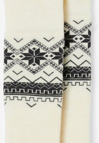 Crème sokken met een zwart geometrisch patroon met zigzags en motieven aan de bovenkant. Gemaakt van een zachte, gebreide stof.