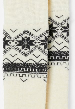 Calze crema con un motivo geometrico nero, caratterizzate da zigzag e motivi nella parte superiore. Realizzate in un morbido tessuto lavorato a maglia.