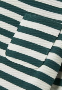 Grön- och vitrandig tyg med en texturerad ribbad mönster, med en liten patchficka på vänster sida.