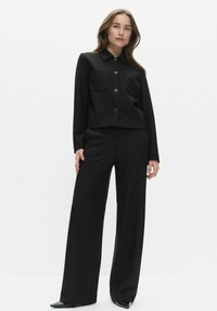 Czarny dwuczęściowy zestaw składający się z koszuli z kołnierzykiem z dwiema przednimi kieszeniami oraz długich, szerokich spodni. Gładka faktura i dopasowany krój.