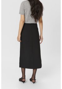 Jupe midi noire avec taille ajustée, poche latérale et fente arrière, assortie à un haut gris à manches courtes. La tenue présente des textures lisses.