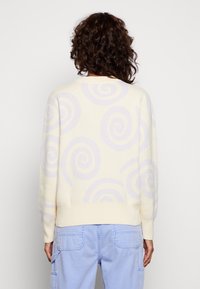 Cremfarbene Pullover mit helllila Wirbelmustern, gerippten Bündchen und Saum sowie einer lässigen Passform, kombiniert mit hellblauen Cargo-Hosen.