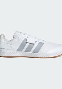 Chaussure de sport blanche avec des rayures grises, fermeture lacée et bande auto-agrippante, semelle texturée et design profilé sur un fond uni.