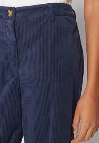 Námořnické kordové kalhoty s vertikálními pruhy, s knoflíkovým zapínáním a pasem. Hladká texturou a přiléhavý střih.