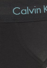 Schwarze Unterwäsche aus einem weichen Material mit einem breiten gestrickten Bund, der das "Calvin Klein"-Logo in Hellblau trägt.