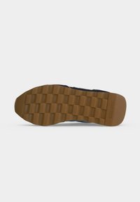Semelle de chaussure en caoutchouc marron avec un motif à blocs et le nom de la marque embossé près du talon sur un fond gris uni.