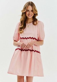 Różowa krótka sukienka z bufkami, ozdobiona czerwoną lamówką na talii i u dołu. Gładki materiał z marszczonym dołem.