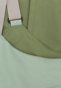 Hellgrüne Tasche mit glatter Textur und geschwungener Form, ausgestattet mit beigen Trägern und schwarzer Hardware zur Längenverstellung.