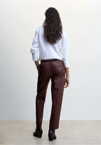 Brown faux leather pants with a relaxed fit, featuring a solid color, elastic waistband, and side seam pockets, paired with a white shirt.