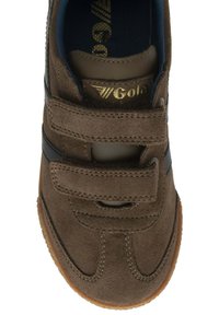 Zapato de ante marrón con acentos en azul marino y dos tiras de velcro. Cuenta con suela de goma y logotipo dorado bordado en el lateral.