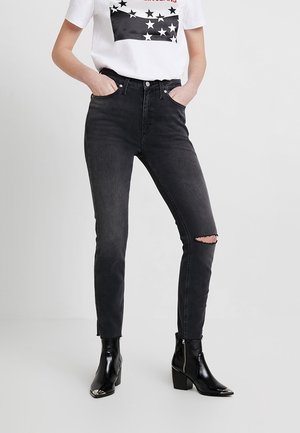 Jeans negros de cintura alta con una rodilla rasgada, combinados con una camiseta gráfica blanca que presenta un patrón de estrellas negras. Botines negros.