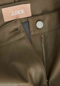 Pantalones de cuero verde oliva con una cremallera visible, un cierre de botón y una etiqueta que dice "JJXX". Presentan una superficie texturizada y un diseño minimalista.