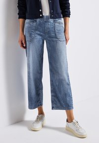 Pantalons en denim bleu clair coupés avec une taille élastique, dotés de poches avant et d'un délavage, associés à des baskets blanches.