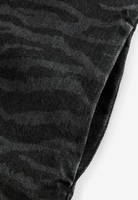 Tissu en denim noir présentant un motif texturé subtil, avec des coutures visibles et une bordure lisse. Vue rapprochée des détails de la surface.
