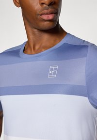 Lyseblå treningstrøye med horisontale striper i varierende nyanser. Laget av pustende stoff, med en liten hvit Nike-logo og rund halslinning.