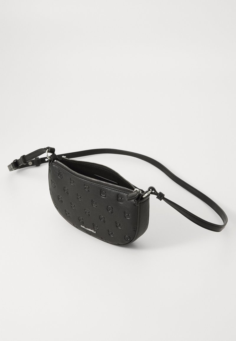 Sac en cuir noir en bandoulière avec un motif de skull en relief, forme ovale, fermeture zippée et sangle réglable. Éléments en métal argenté.