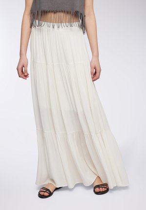 Gonna maxi bianca a strati realizzata in tessuto leggero. Presenta una silhouette fluida ed è abbinata a sandali neri con cinturini.