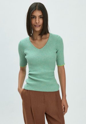Maglione a coste verde menta con scollo a V e maniche corte, caratterizzato da una vestibilità slim e un tessuto texture. Abbinato a pantaloni marroni.