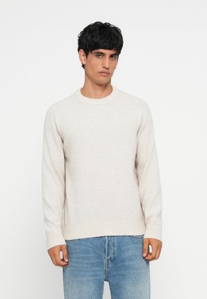 Light beige sweater with a round neck, ribbed cuffs and hem, and a soft texture. Worn with blue jeans, featuring a straight fit.