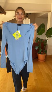 Sinine pikkade varrukatega bodi, mis on valmistatud pehmest kangast, millel on ümara lõikega kaelus, ja millel on hooldusjuhiste silt ning brändi label.