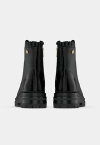 Schwarze Knöchelstiefel mit glatter Oberfläche, Rüschensaum, goldenen Akzenten und einer robusten Sohle mit strukturierten Details.