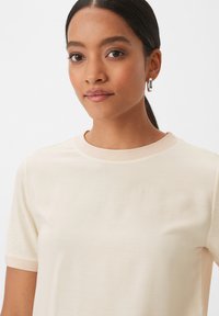 T-shirt a maniche corte color crema con scollo rotondo. Tessuto morbido, vestibilità leggermente rilassata e dettagli di cucitura discreti sul colletto.