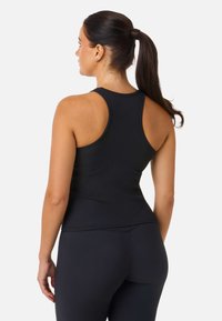Svart ribbad linne med racerback-design, figurnära passform och mjuk textur. Kombinerat med helsvarta leggings för en koordinerad look.