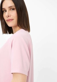 Kortærmet, rundhalset bluse i blødt lyserødt stof, med afslappet pasform og glat tekstur; vist på en model med glat hår.
