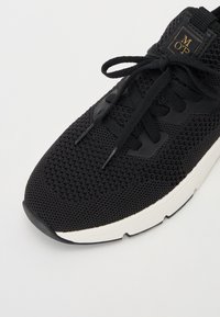 Musthave mustrehanak mustmustiga kootud ülemise, lame paelade ja valge vaheosaga must mesh toss. Tootel on väike kuldne logo keele lähedal. Ümar varvas.