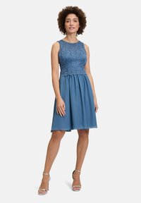 Blauwe jurk met een kanten lijfje en een vloeiende chiffon rok. Mouwloos met een ronde halslijn. Zilveren gekruiste hakken vullen de outfit aan.