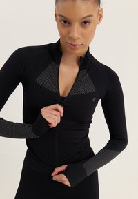 Black athletic zip-up jacket with textured mesh panels on shoulders and sleeves; fitted design with long sleeves and thumbholes.