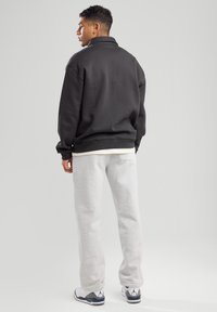 Black sweatshirt with high collar, gray sweatpants, and white sneakers with gray accents. Casual fit, smooth fabric, simple design.