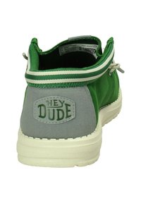 Scarpa slip-on in tessuto verde con tacco in tessuto grigio, suola bianca e collare a righe verde e bianco. Presenta il logo "HEY DUDE" sul tallone.