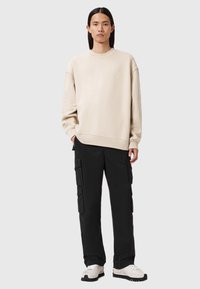 Felpa beige a girocollo, taglio oversize, tessuto testurizzato. Abbinata a pantaloni cargo neri con tasche laterali. Sneakers bianche con suole nere.
