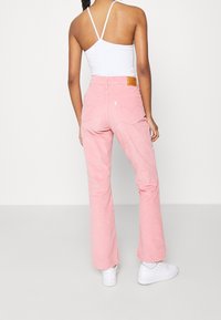 Różowe spodnie w stylu dzwonów z dżinsowego materiału, z tylnymi kieszeniami i skórzaną metką marki. Połączone z białym topem na ramiączkach i białymi sneakersami.