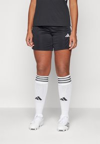 Black athletic shorts with a smooth texture, paired with white knee-high socks featuring black stripes and black cleats.