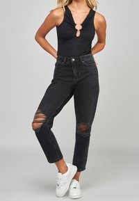 Svart ribbad bodysuit med nyckelhålsdetalj och ärmlös design, matchad med högmidjade svarta slitna jeans med rivna knän.