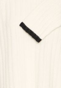 Tejido de suéter blanco con superficie texturizada. Los detalles en negro en el puño añaden contraste al diseño general.