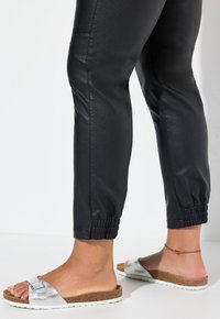 Pantaloni jogger neri in ecopelle con polsini elasticizzati, abbinati a sandali con fibbia e suola in sughero di colore argento.