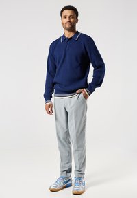 Námořnický pletený svetr s límcem a pruhovanými manžetami, spárovaný se světlými šedými kalhotami a stříbrnými teniskami s modrými akcenty.