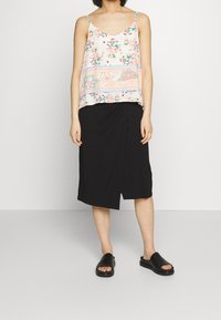 Květinová tílko vyrobené z lehké, vícebarevné látky; spárované s černou drapovanou sukní ke kolenům a černými skluzavkami.