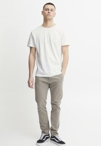 White cotton t-shirt, relaxed fit. Light beige pants, slim design. Black sneakers with white accents, low-top style. Casual ensemble.